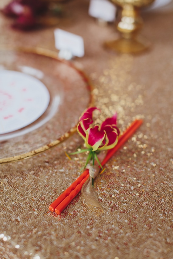 Gloriosa lily accent on red chopsticks on gold sequin linen. Red and gold dinner party inspiration. See more at Rebecca Chan Weddings and Events https://www.rebeccachan.ca